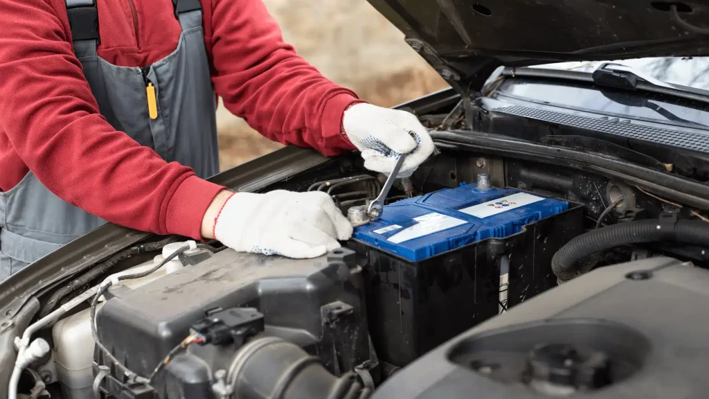 Mechanic working under the hood showing how to stop a car battery from draining by tightening battery terminals