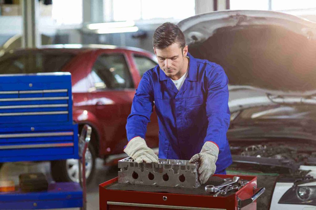 A man in blue overalls works diligently on a car, focusing on the battery replacement task as part of vehicle maintenance.