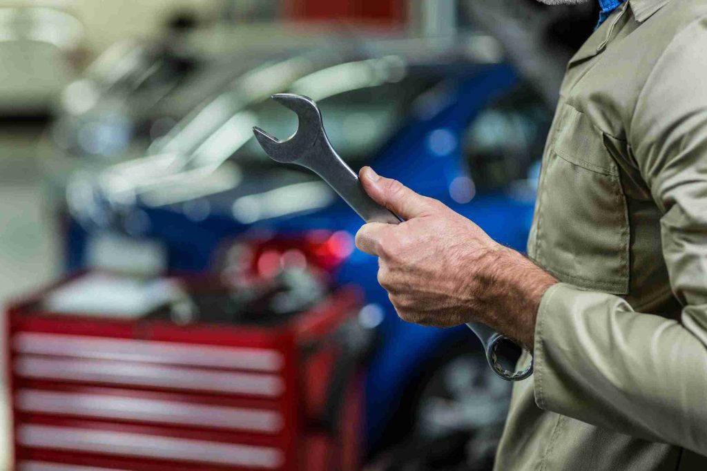 A man holds a wrench, prepared to assist with same-day mobile auto repairs beside a car.