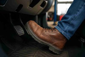 Mechanic pressing a car brake pedal during inspection in a professional workshop, showing why a brake pedal feels spongy